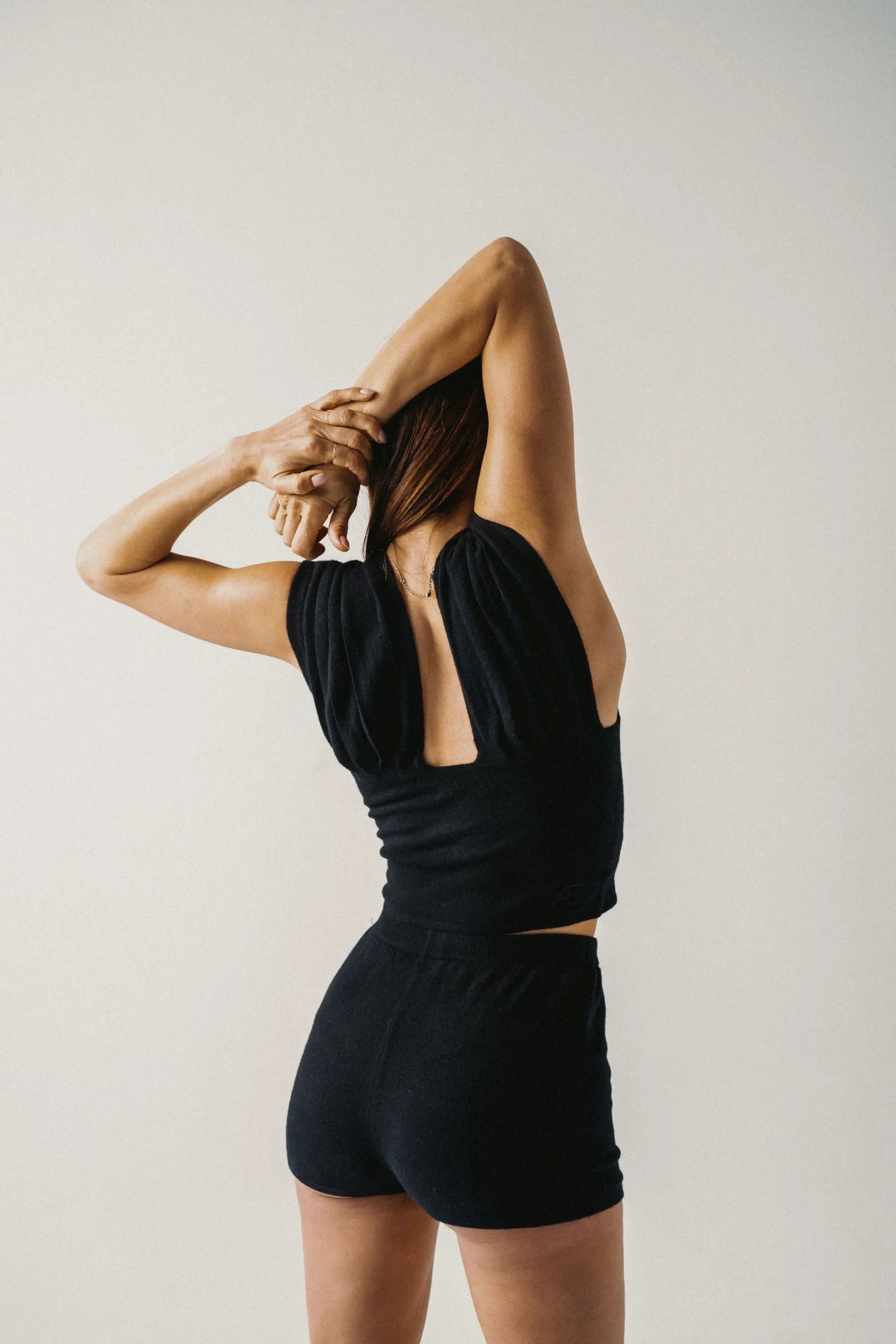 Woman wearing a black top and mini short against a plain background