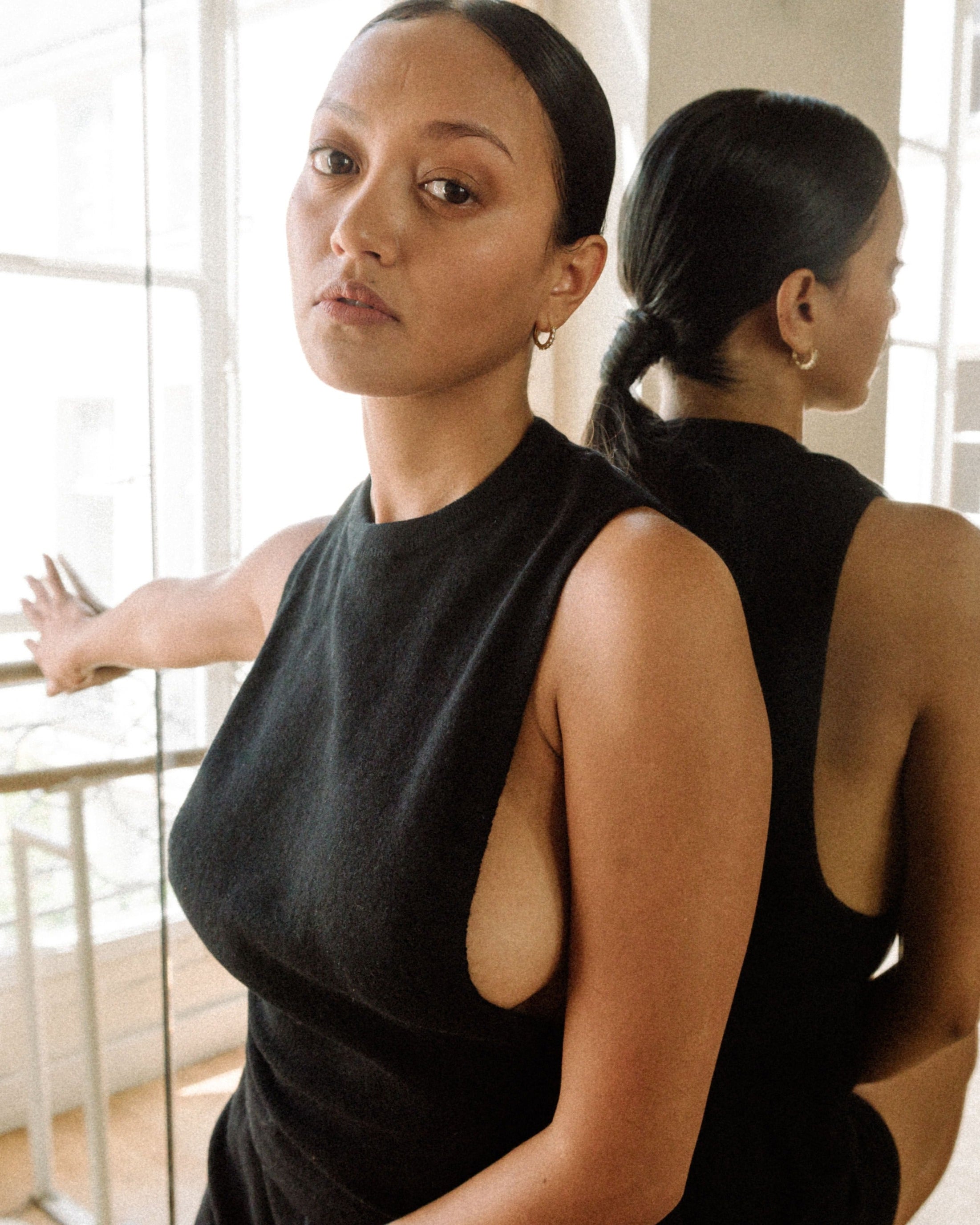 Woman wearing a black sleeveless top with side opening detail facing a mirror