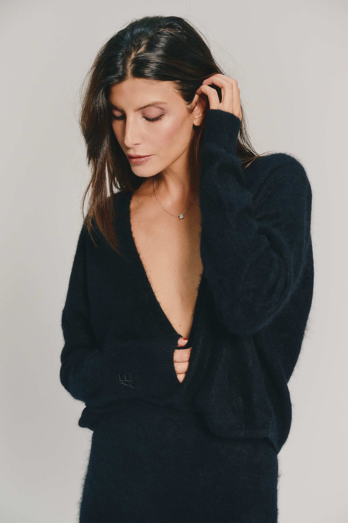 A woman wearing a back brushed cashmere cardigan with a very deep V-neckline, posed against a neutral light gray background.