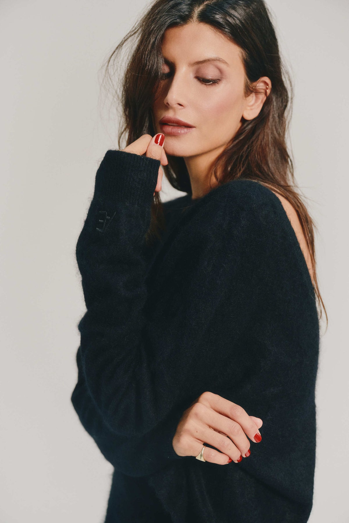 A woman wearing a black brushed cashmere sweater with a shoulder cutout, posed against a light gray studio background.
