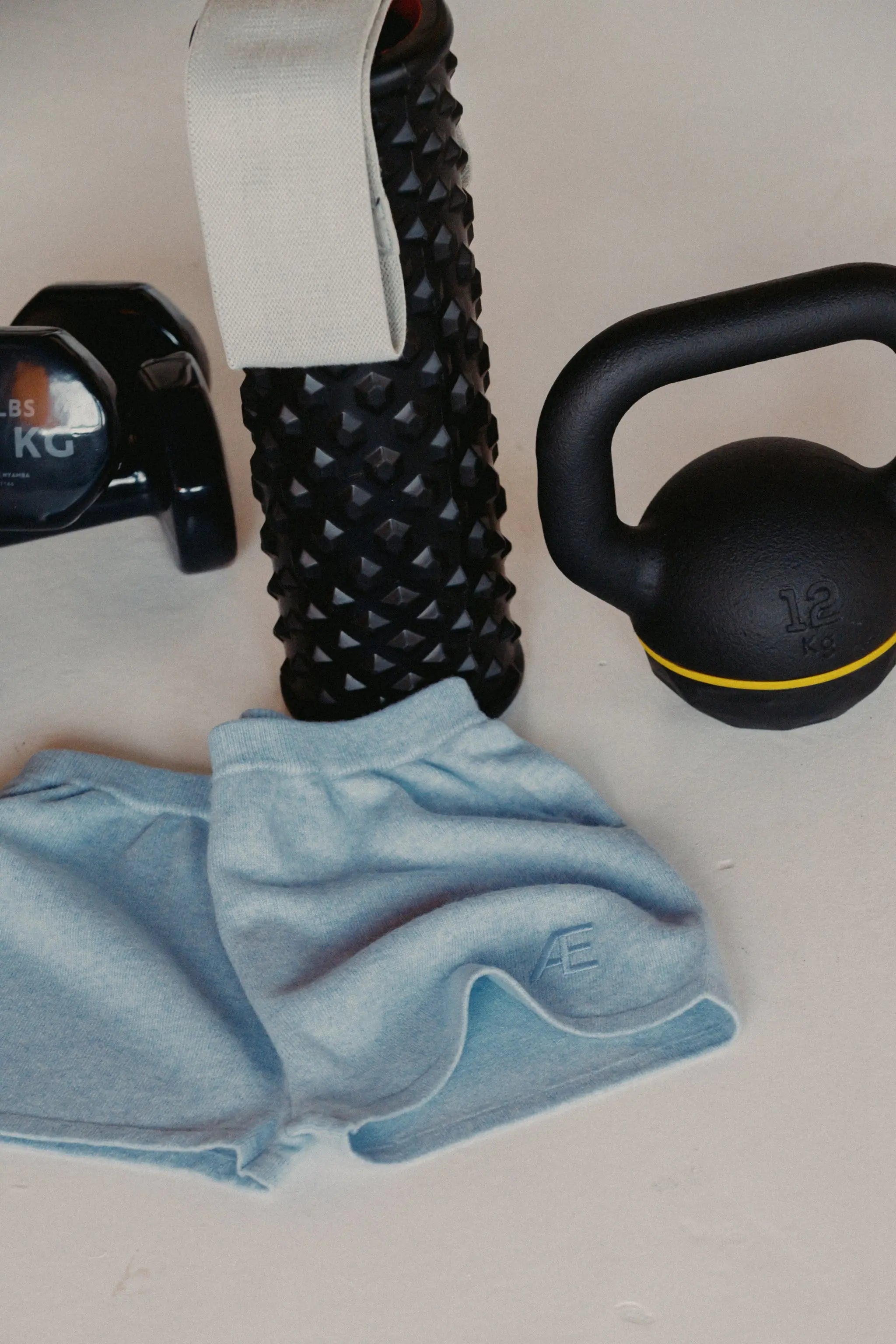Black massage roller, blue mini short, and black kettlebell on a light surface