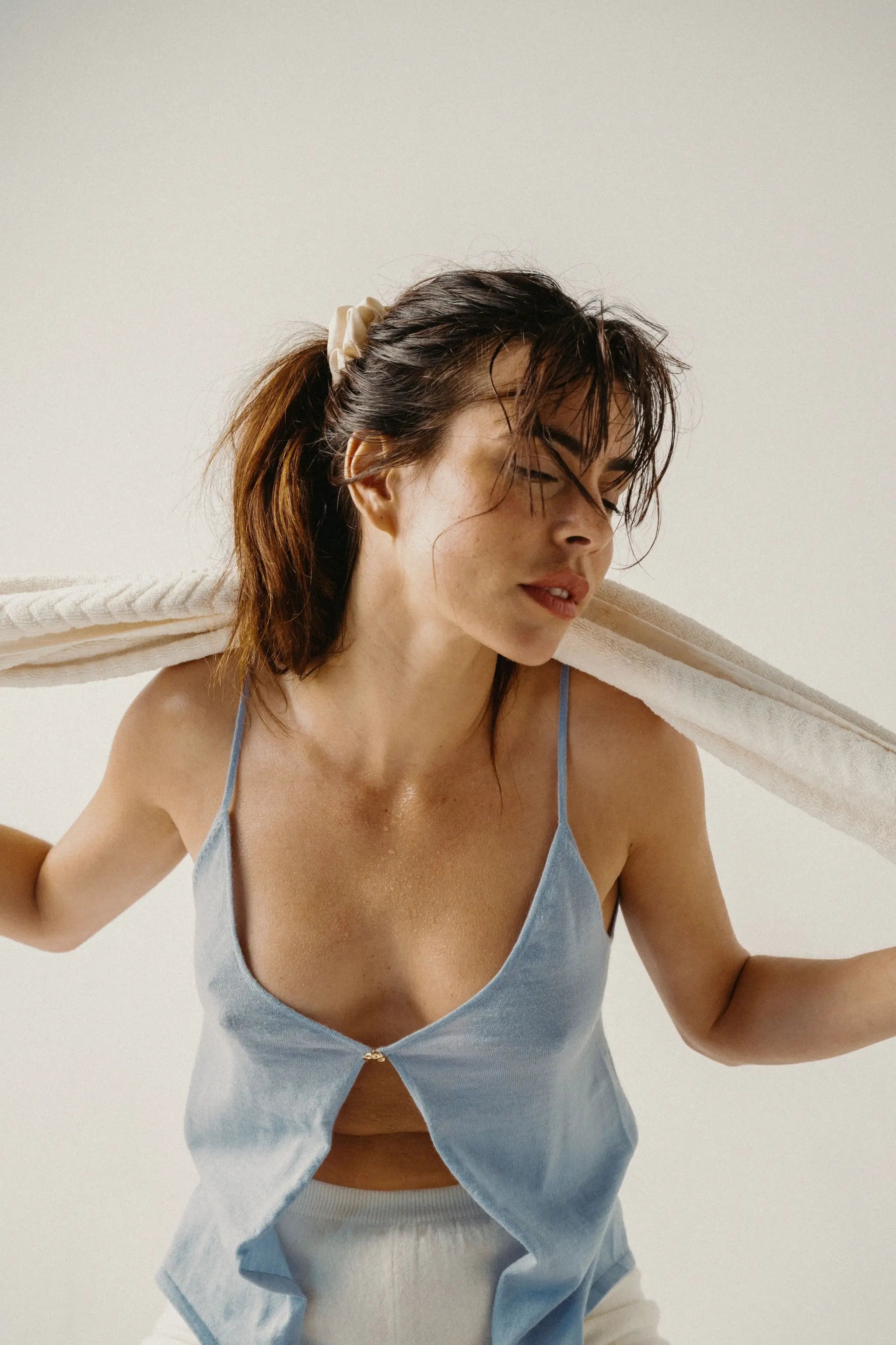 Woman wearing a light blue reversible top with jewel button detail, against a white background