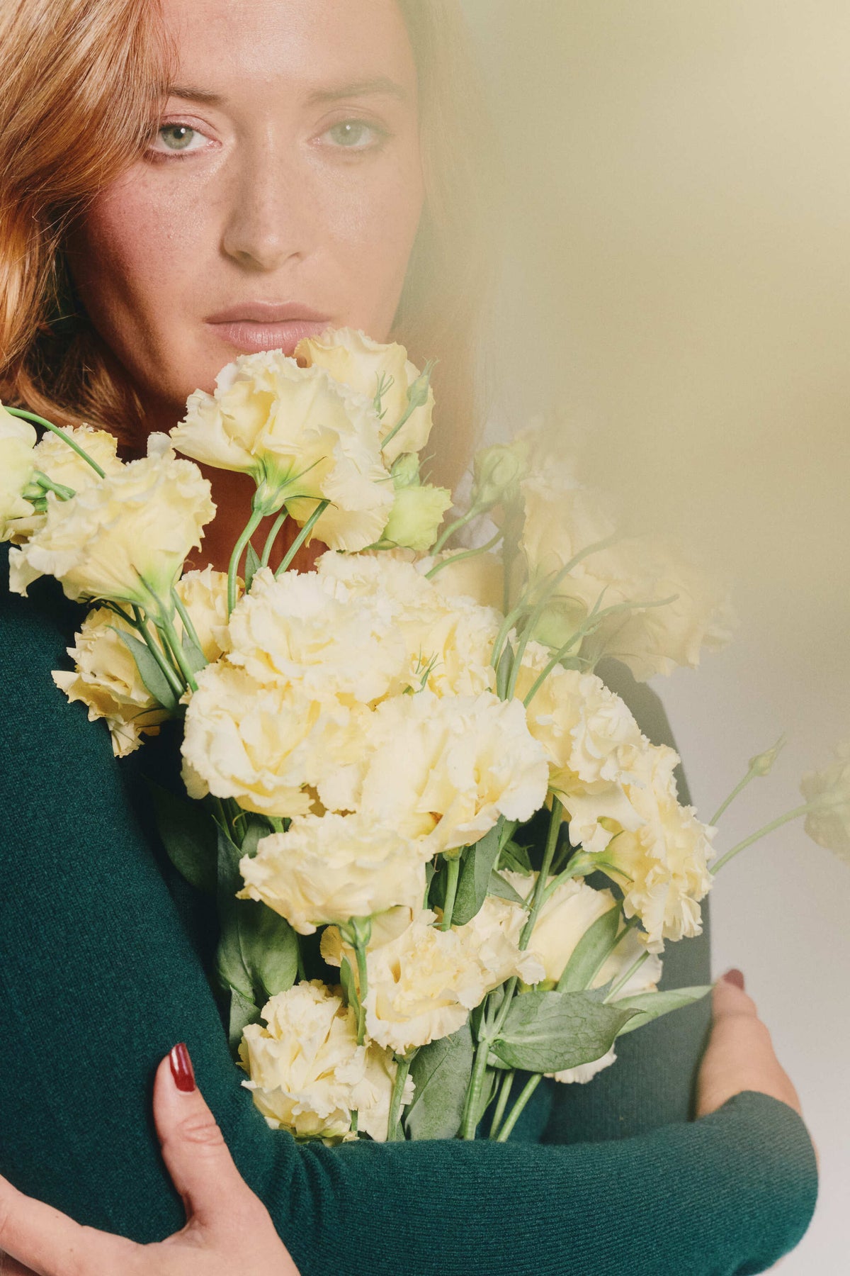 red hair women wearing a green body in cashmere, looking straight at the camera, holding ivory flowers