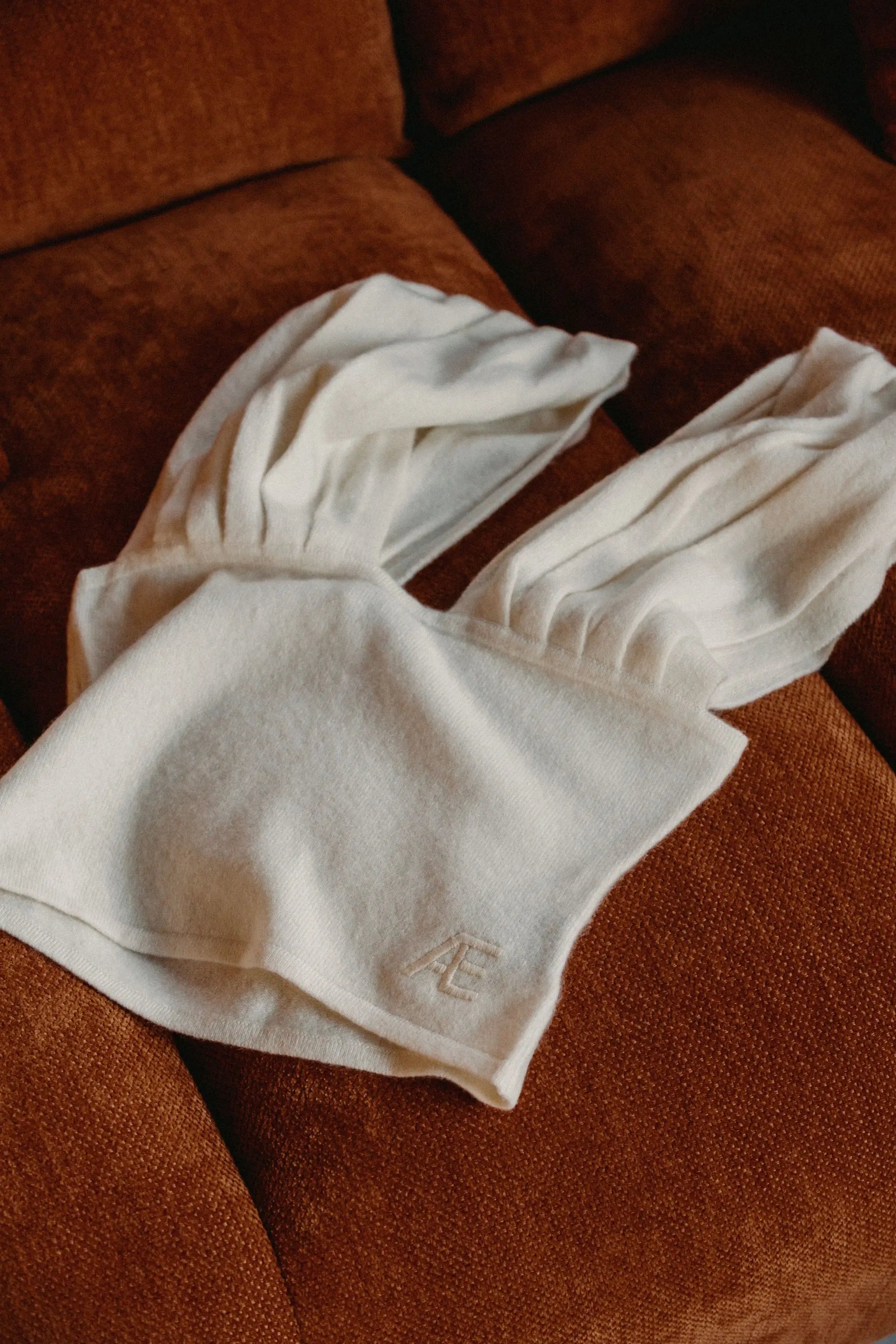 White cashmere top laid on a rust-colored sofa