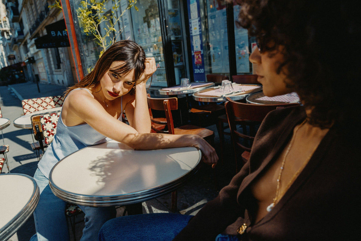 Two women sitting at a table in an outdoor cafe setting.