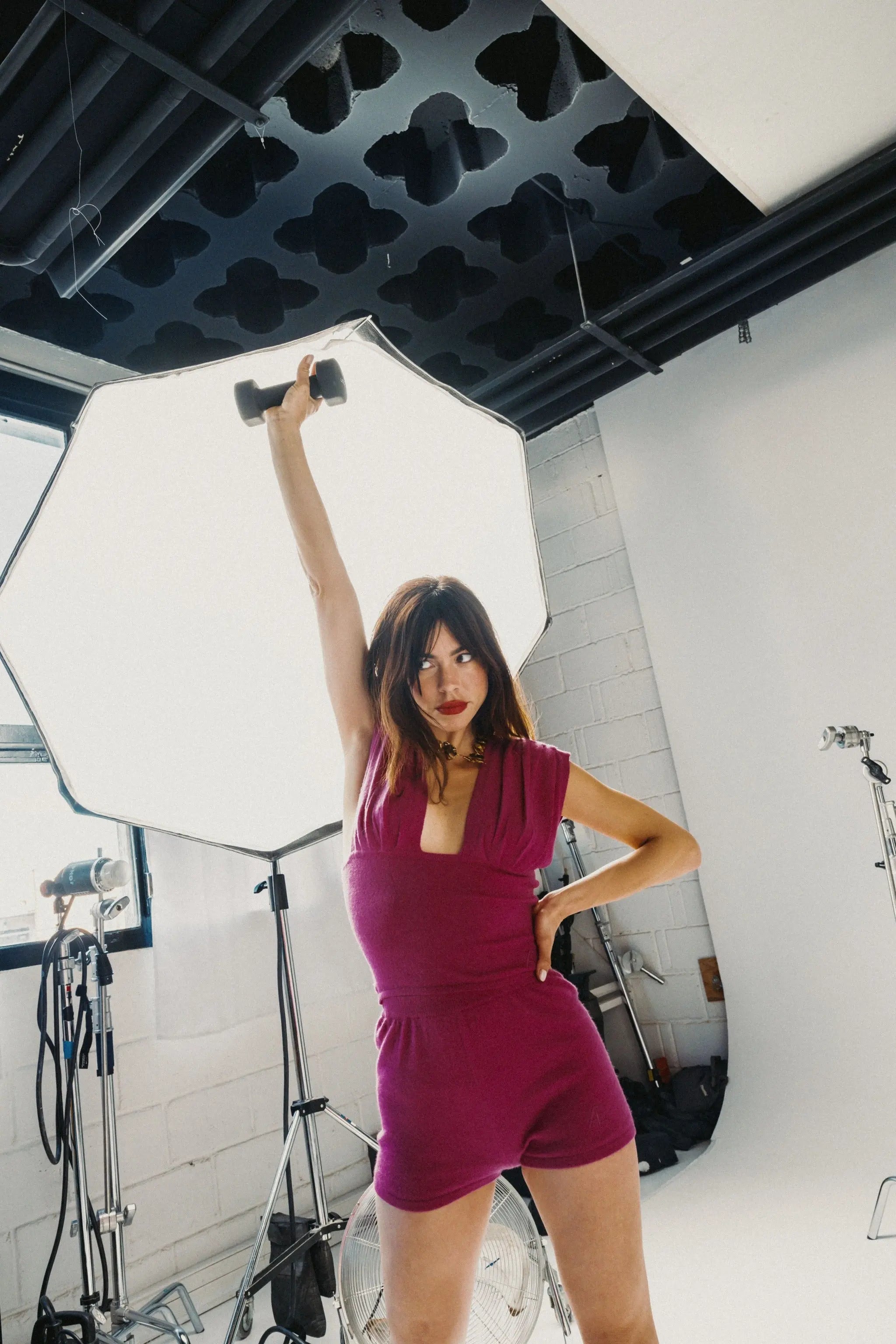 Woman in a pink outfit posing in a studio with photography equipment.